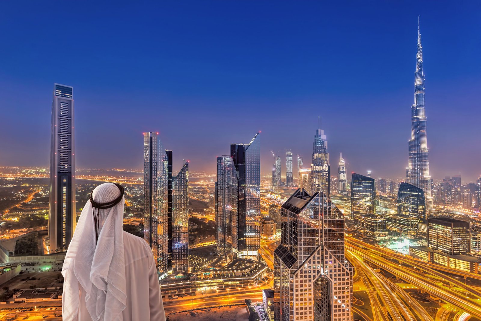 Arabian man watching night cityscape of Dubai with modern futuristic architecture in United Arab Emirates